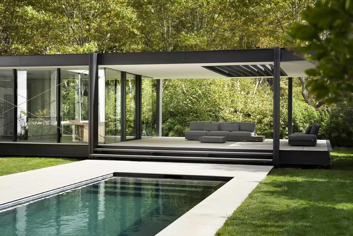 Modern minimalist glass pool house with sleek black framing and outdoor lounge area, surrounded by lush greenery, perfect for contemporary outdoor living and design.