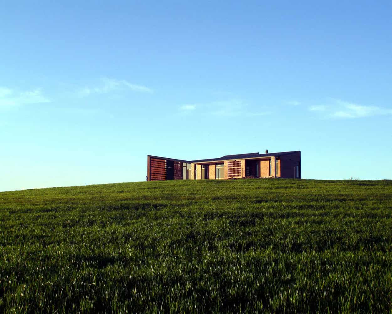 Modern minimalist house on a grassy hill under a clear blue sky, showcasing innovative architecture and sustainable design.