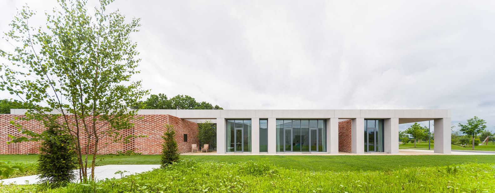 Contemporary modern house with clean lines and large glass windows, surrounded by lush green lawn and trees, showcasing minimalist architectural design and outdoor seating area.