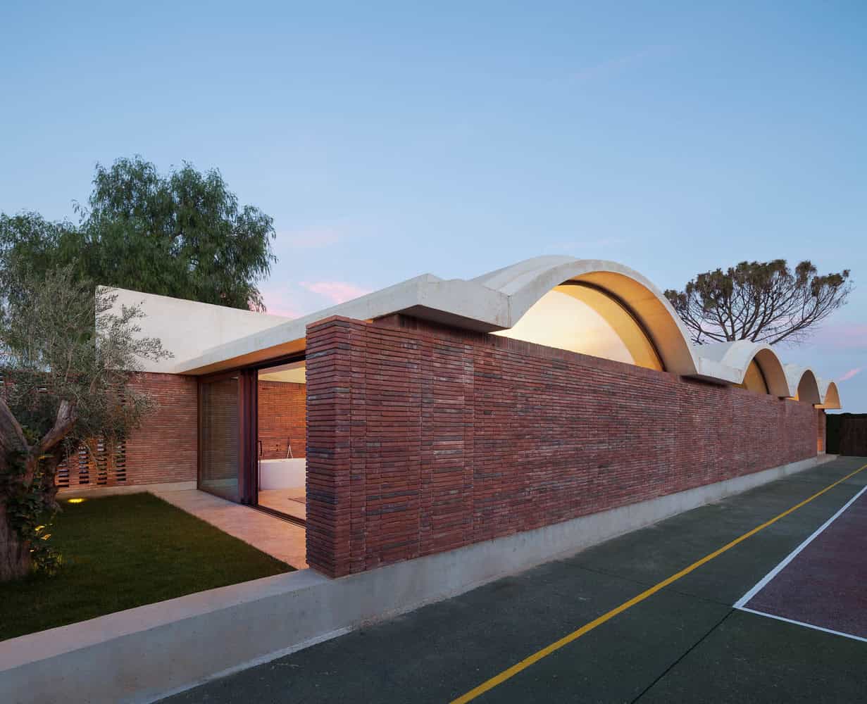 Red brick building with arched concrete roof design, modern architecture, contemporary house exterior, innovative roofing, architectural design, art-inspired structure, unique building style, architectural marvel, stylish residential architecture, creative roof design.