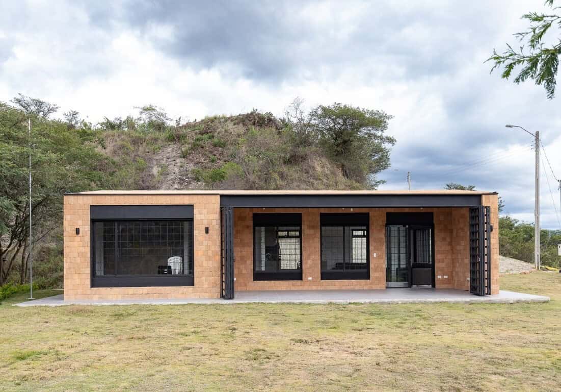 Modern minimalist house with brick exterior, large black-framed windows, and sleek design, set against a natural landscape with hills and trees, showcasing contemporary architecture and innovative design.