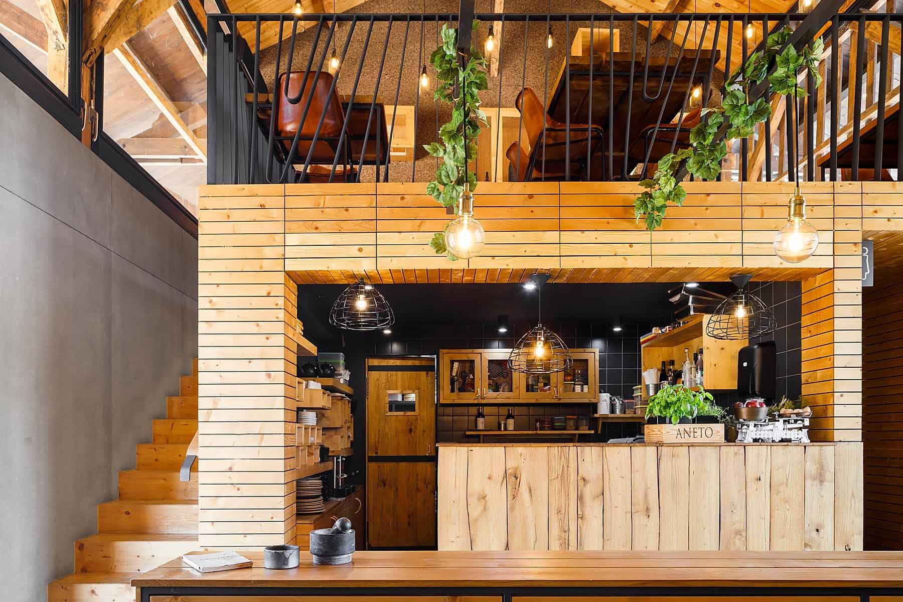 Modern rustic cafe interior with wooden finishes, black accents, hanging pendant lights, and lush greenery, showcasing warm and inviting architecture and interior design elements.