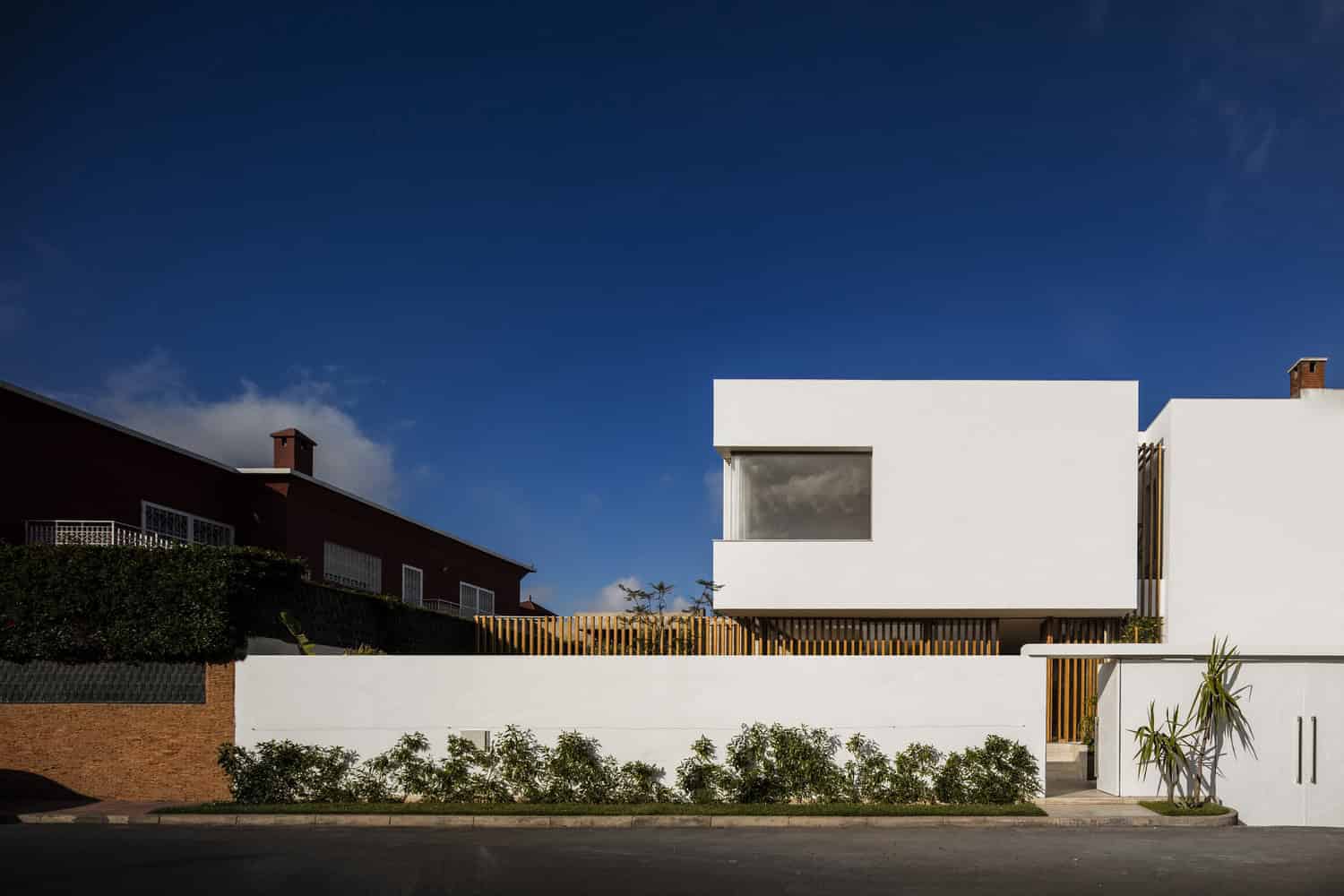 Contemporary minimalist white house with geometric design and large window, modern architecture art, clean lines, and wooden fencing, set against a clear blue sky.