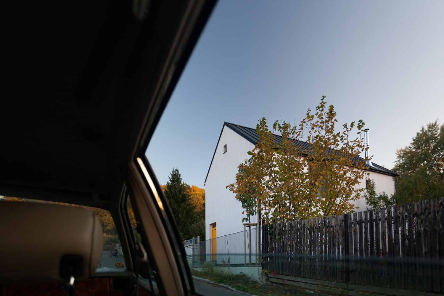 Modern minimalist white house with black roof and autumn foliage, showcasing contemporary residential architecture and exterior design.