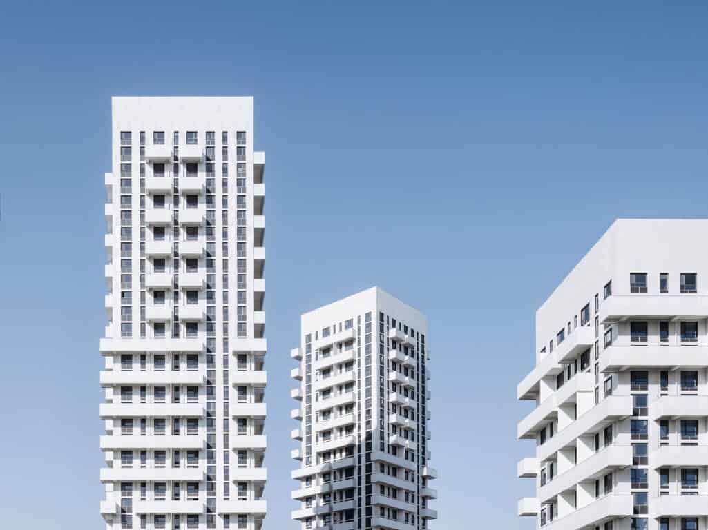 Luxury modern white high-rise apartment buildings with geometric design against a clear blue sky.