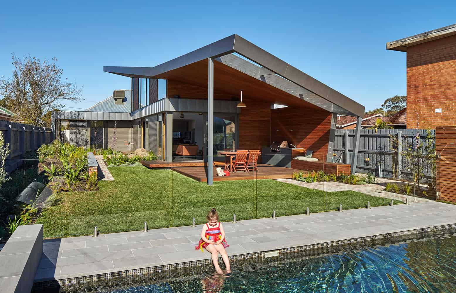 Contemporary modern backyard with luxurious pool, outdoor deck, and sleek architectural design featuring wood accents and glass elements for stylish outdoor living.