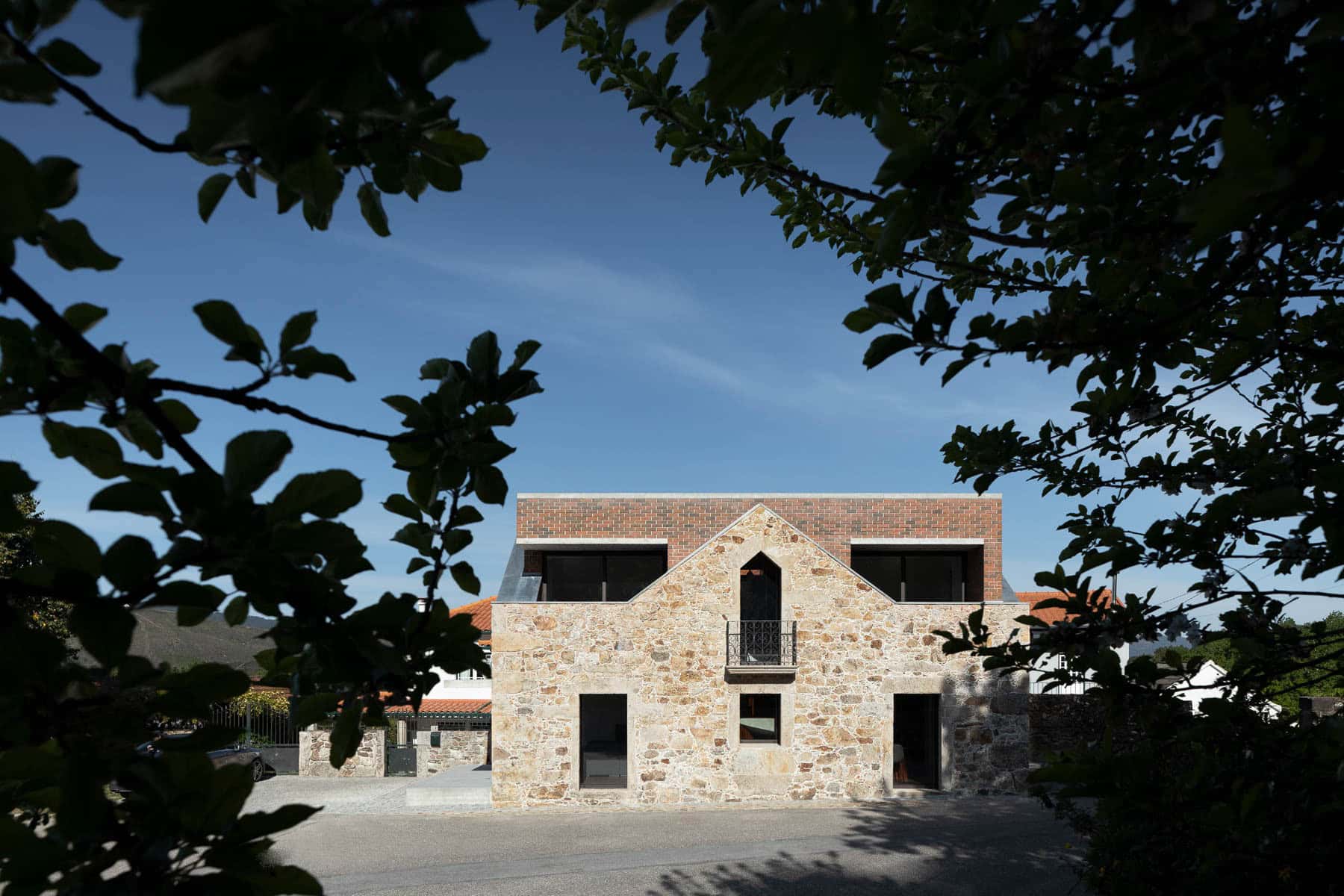 Modern stone and brick house with contemporary architectural design and large windows, framed by greenery, under a clear blue sky.