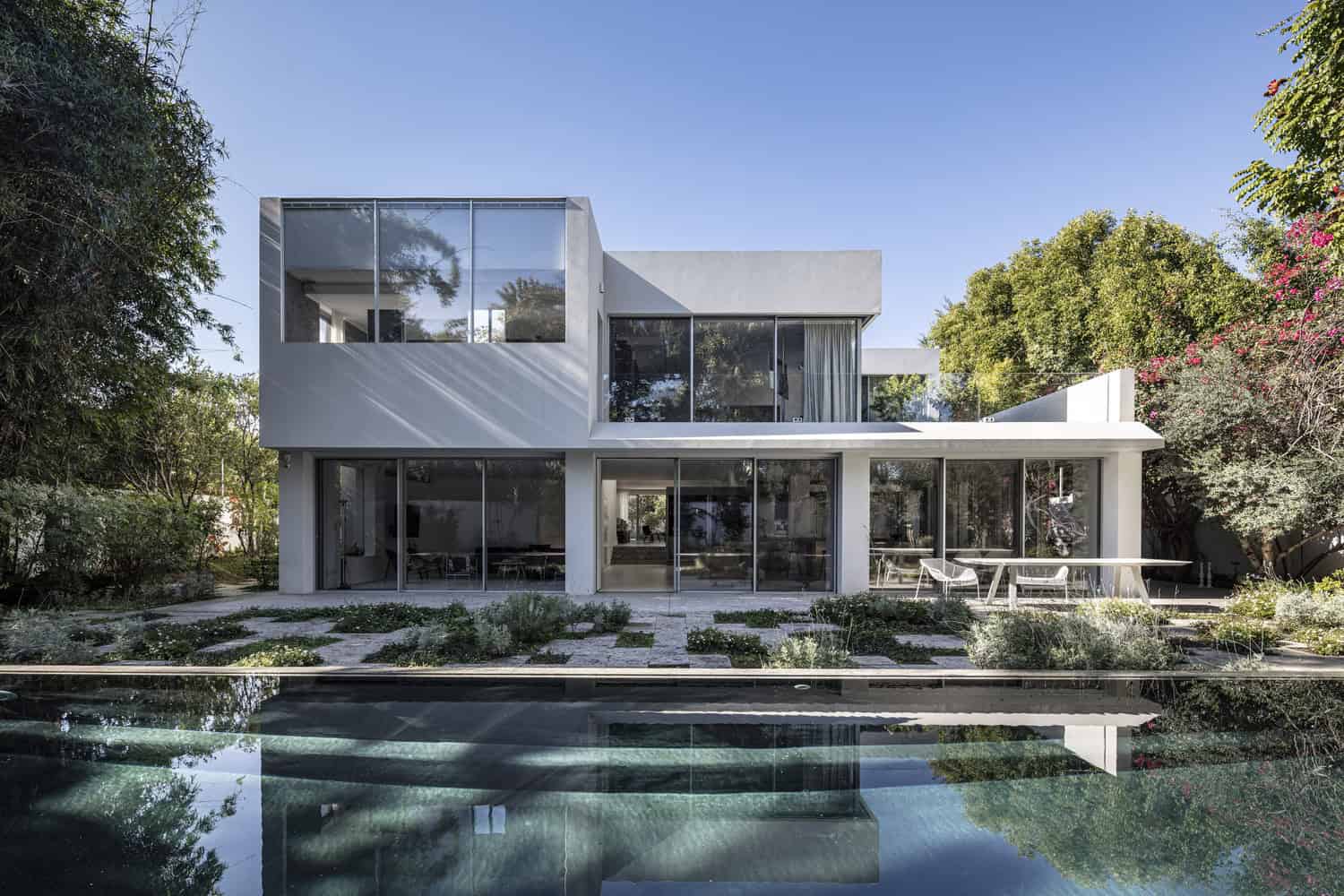 Contemporary modern house with sleek glass walls and minimalist design, surrounded by lush greenery and outdoor pool area. Perfect for modern architecture and stylish home design.