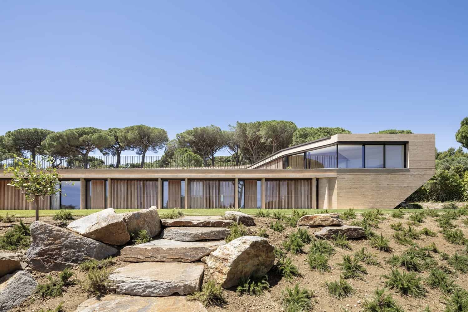 Modern contemporary house with sleek concrete and large glass windows, surrounded by natural landscape and sea views.