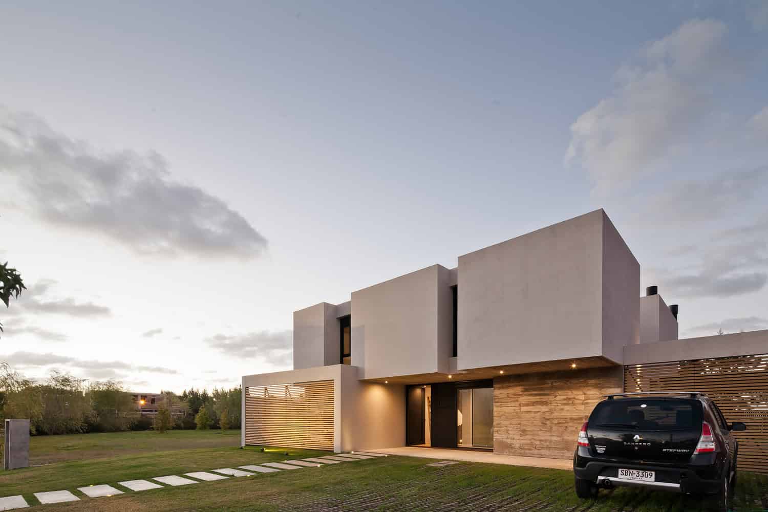 Contemporary modern house with minimalist design, clean lines, and geometric architecture featuring white walls and wooden accents, set against a sunset sky.
