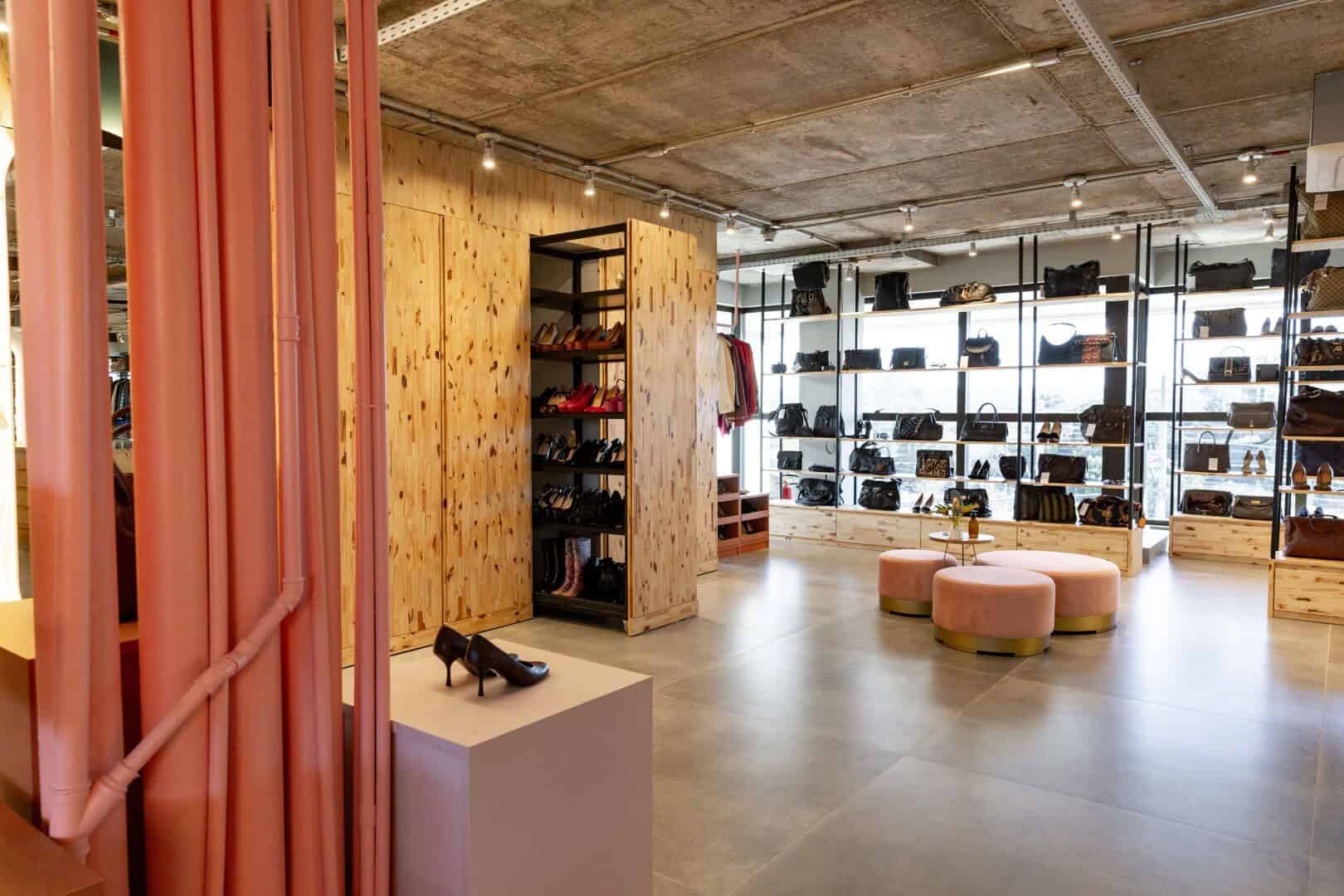 Elegant retail store interior showcasing modern designer handbags, shoes, and accessories with contemporary wooden accents and ample natural lighting, perfect for high-end fashion retail displays.