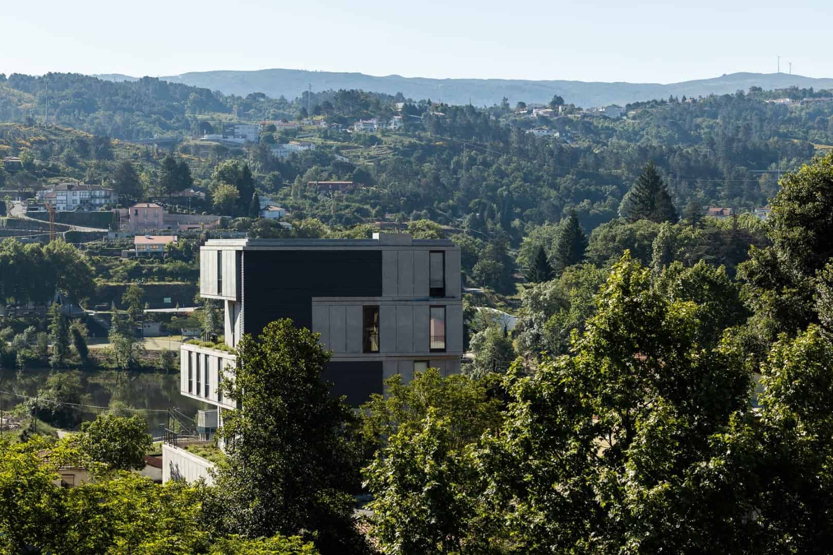Modern minimalist house with geometric design and large windows in a lush green landscape.