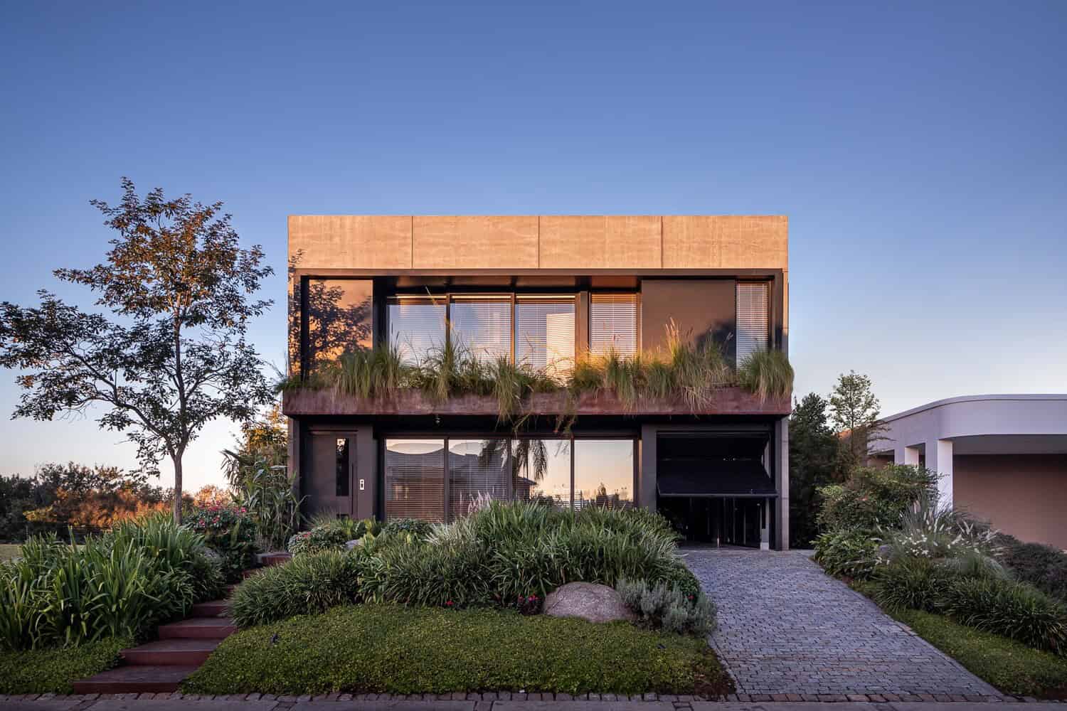 Modern two-story house with contemporary architecture, large glass windows, and lush landscaping around the property.