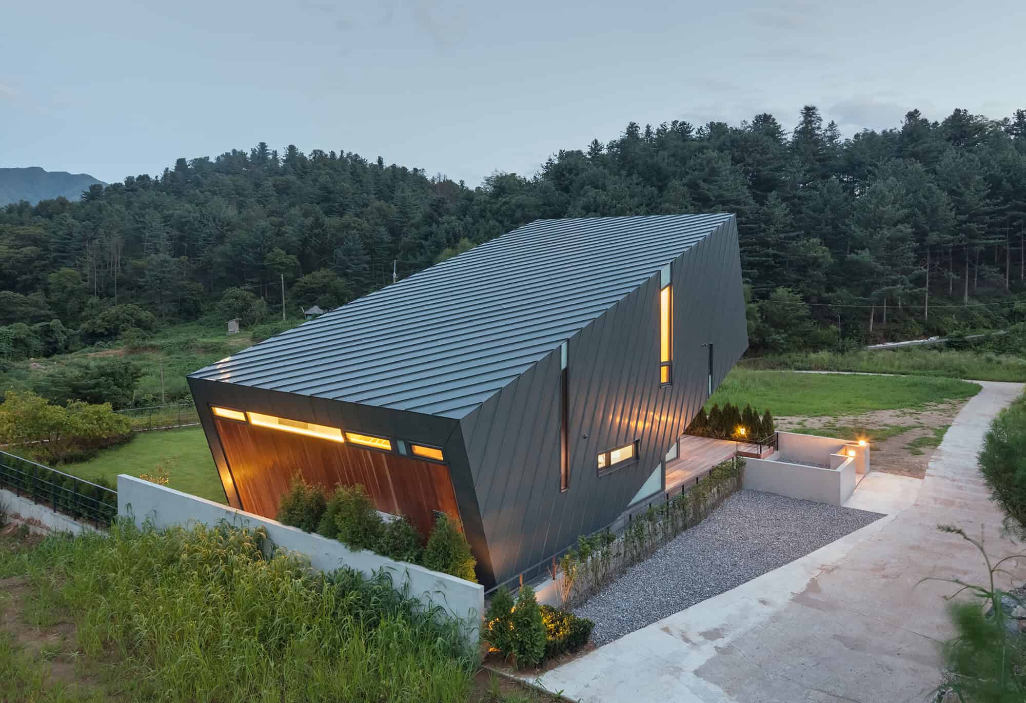 Contemporary modern house with angular design, metal roofing, and large windows set in lush green landscape, showcasing innovative architecture and stylish exterior.