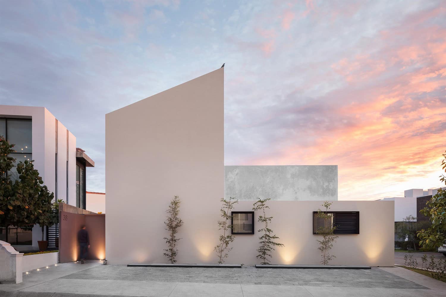 Contemporary minimalist house with sleek white façades, modern architectural design, and landscaped surroundings at sunset.