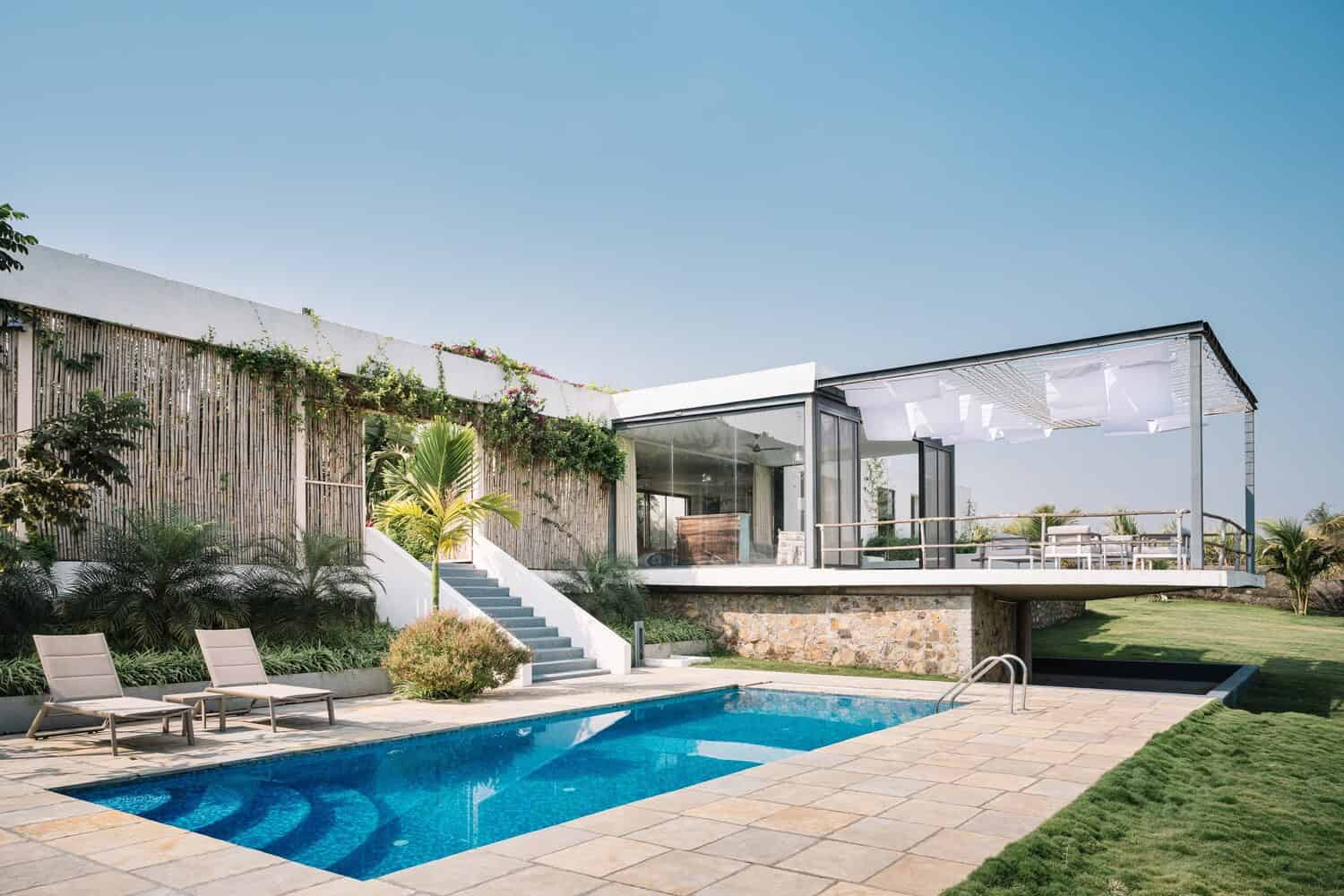 Modern luxury house with a pool, glass walls, outdoor seating, contemporary design, tropical landscaping, and open-plan living area.