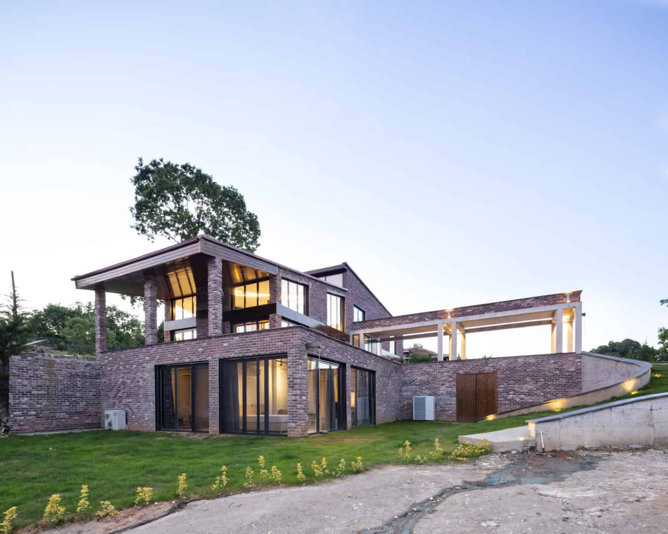 Modern brick house with large windows, open terraces, and contemporary architectural design during sunset.