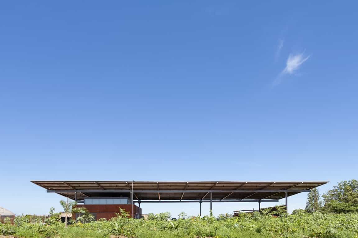 Wide modern architectural pavilion with solar panel roof and open design amidst lush greenery on a sunny day, showcasing contemporary eco-friendly building architecture.