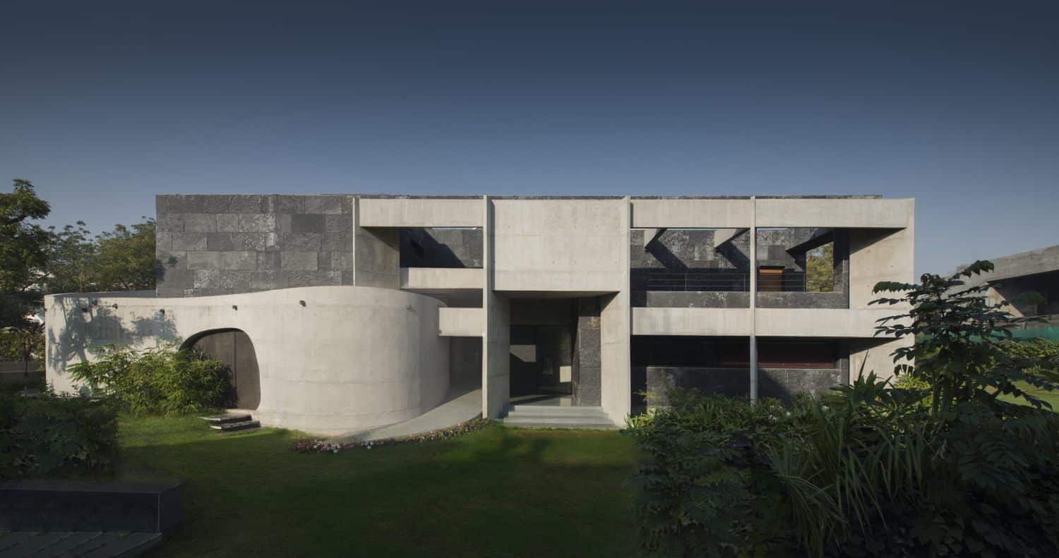 Modern minimalist concrete house with geometric design and lush garden landscaping.