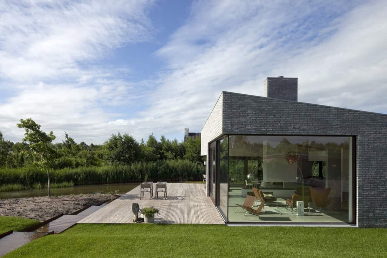 Modern minimalist house with large glass windows and sleek brick exterior in a natural landscape setting.