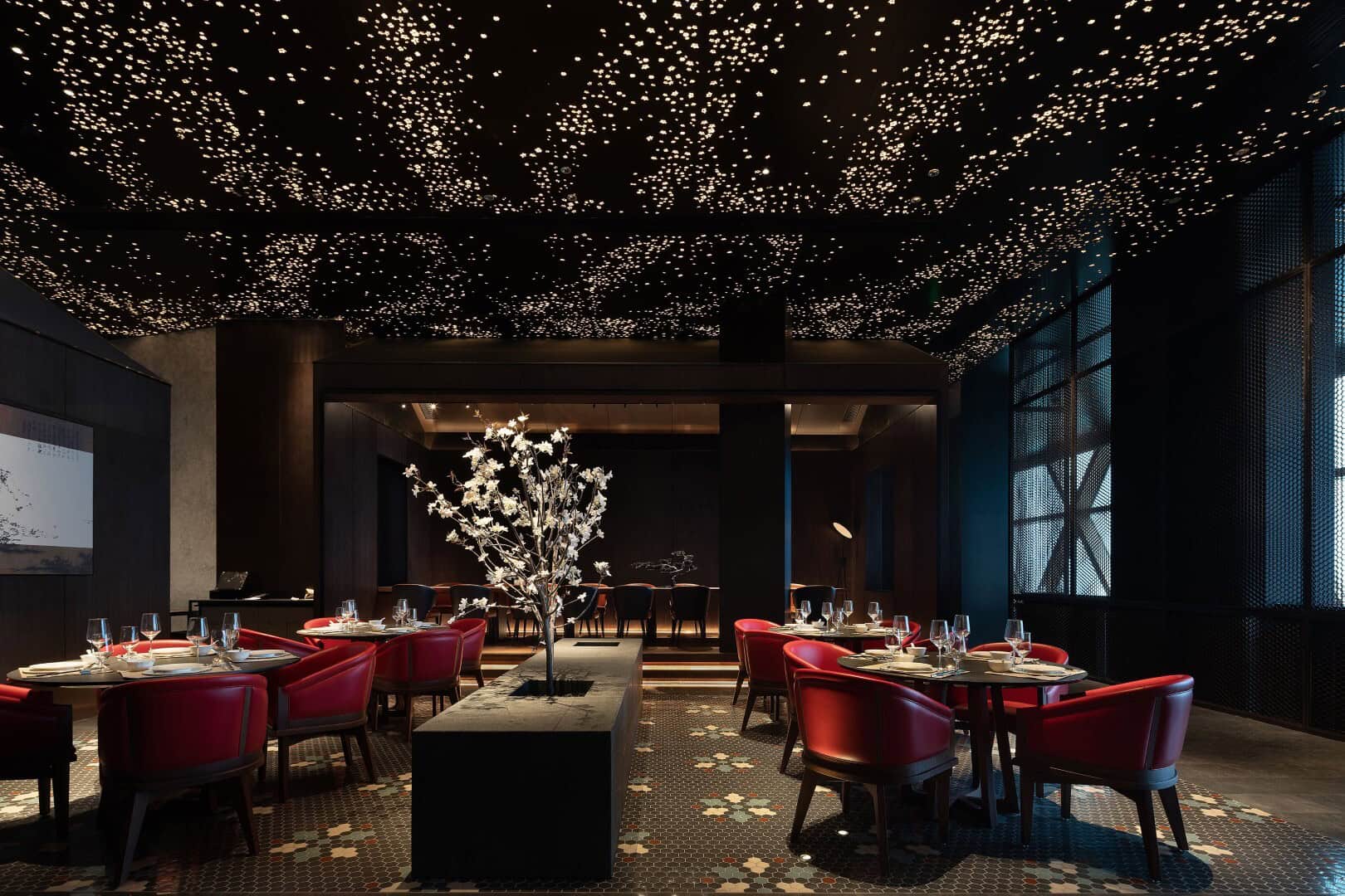 Luxurious modern restaurant interior with starry ceiling lighting, plush red chairs, elegant table settings, and contemporary decor creating an upscale dining atmosphere.