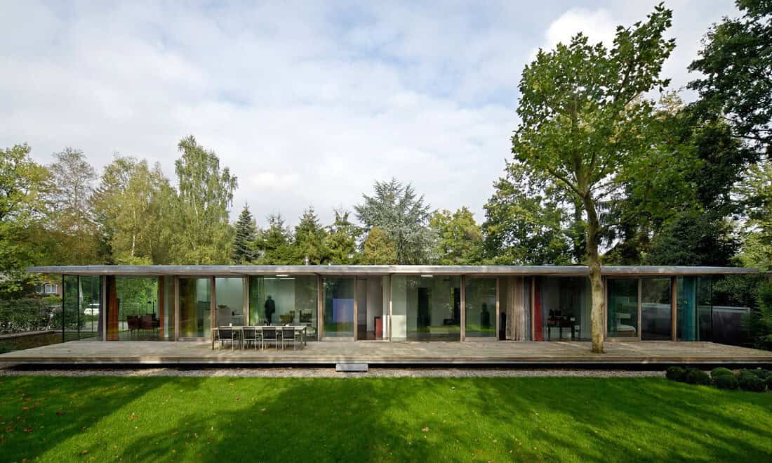 Modern glass house with open-concept design, surrounded by lush greenery and mature trees, highlighting contemporary architecture and innovative use of glass and natural materials.