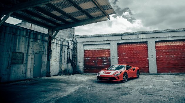 A red Porsche parked below an open carport against a white concrete wall.