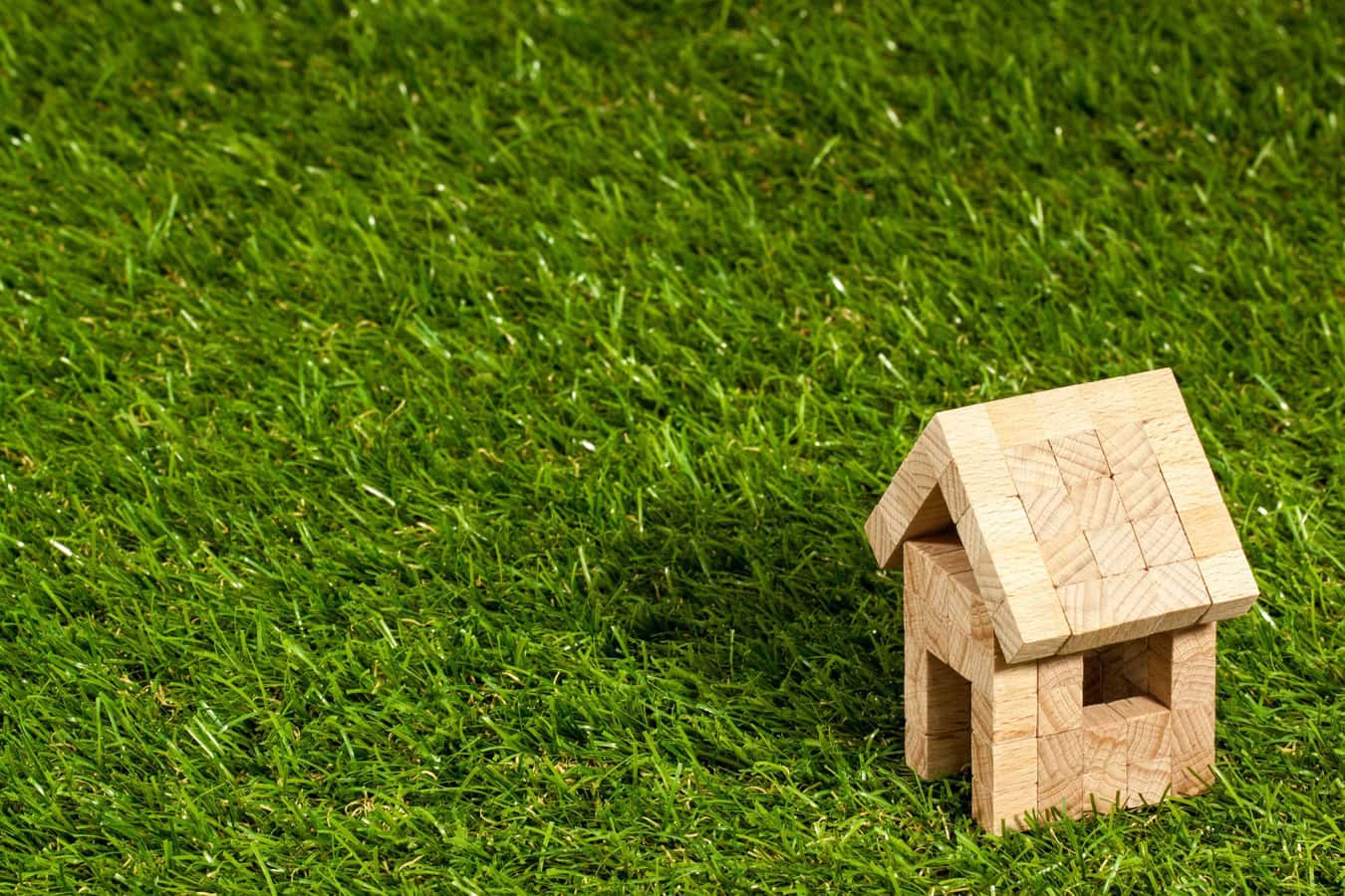 Small wooden house model on lush green grass, symbolizing eco-friendly architecture, sustainable building designs, and outdoor living spaces in modern architecture design.