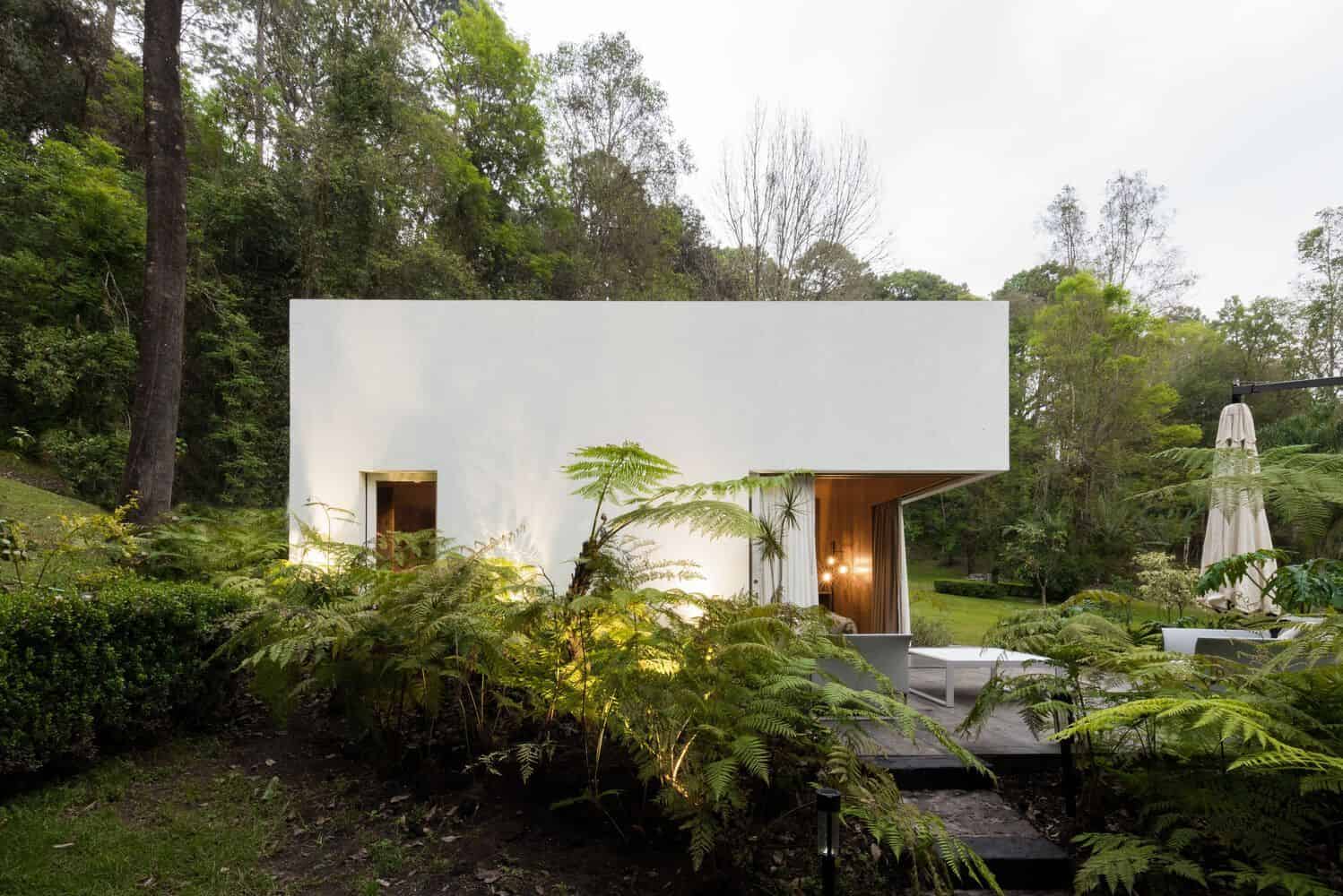 Modern minimalist white house with lush green landscape and outdoor seating area, exemplifying innovative architecture and contemporary design.