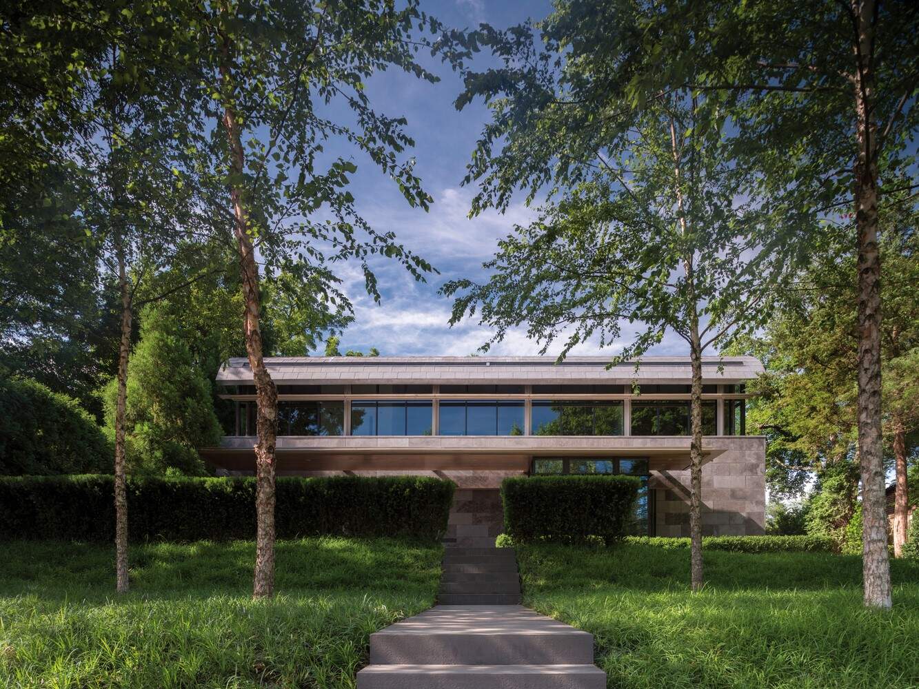 Modern contemporary house with large glass windows, surrounded by lush greenery and tall trees, showcasing minimalist architectural design and sustainable outdoor landscaping.