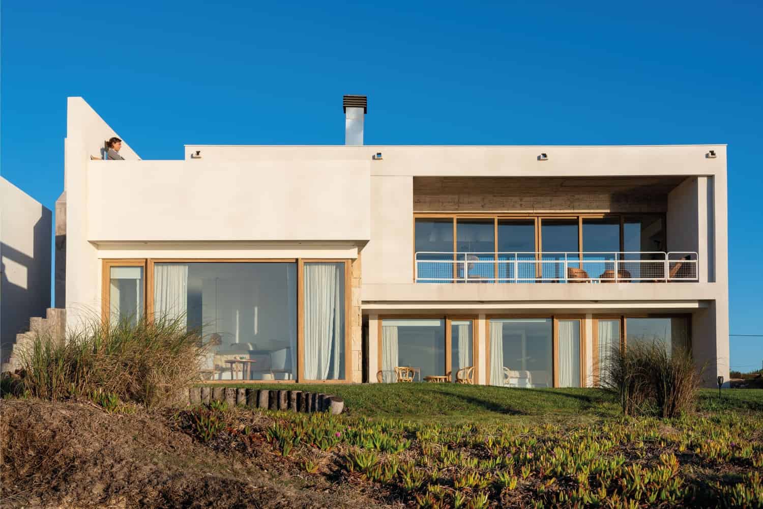 Modern minimalist house with large glass windows and clean white exterior, featuring contemporary architecture and outdoor balcony design.