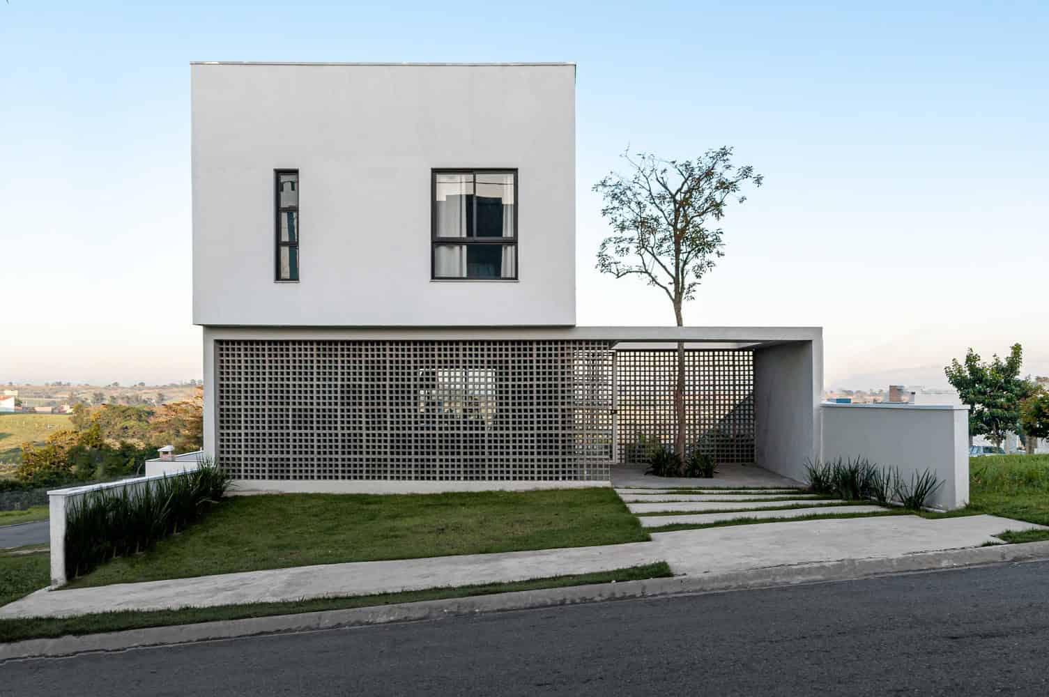 Modern minimalist white house with clean lines and unique architectural elements, including a perforated facade and sleek windows, set against a clear sky.