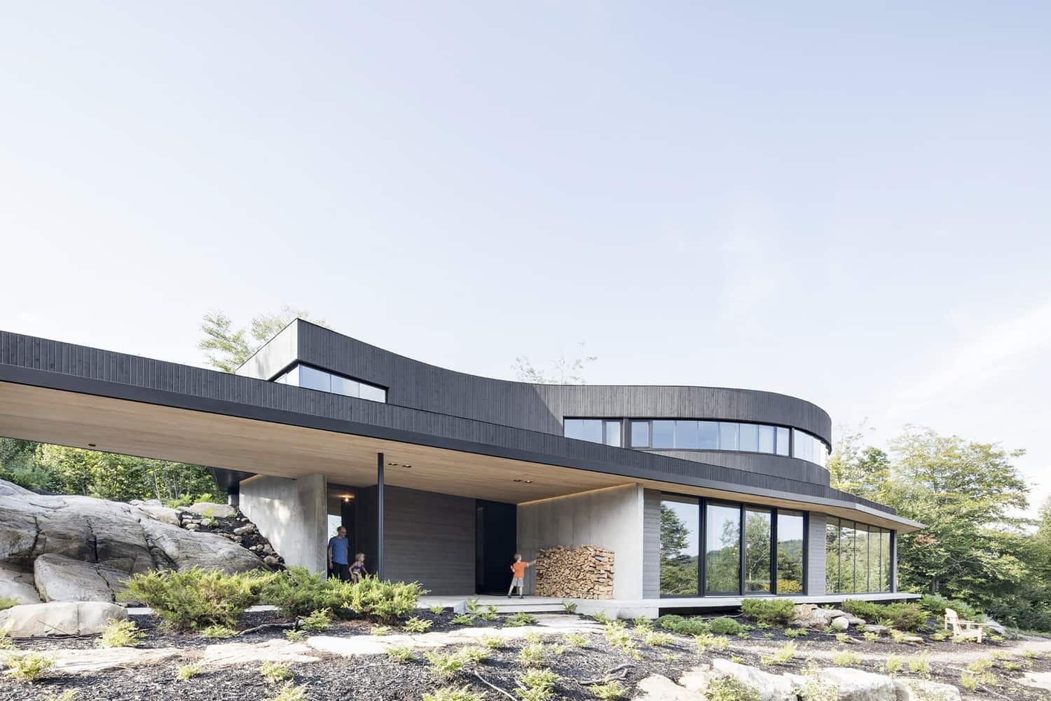 Contemporary modern house with sleek black exterior, large glass windows, and unique curved design, set in a lush natural landscape showcasing innovative architecture and stylish outdoor living spaces.