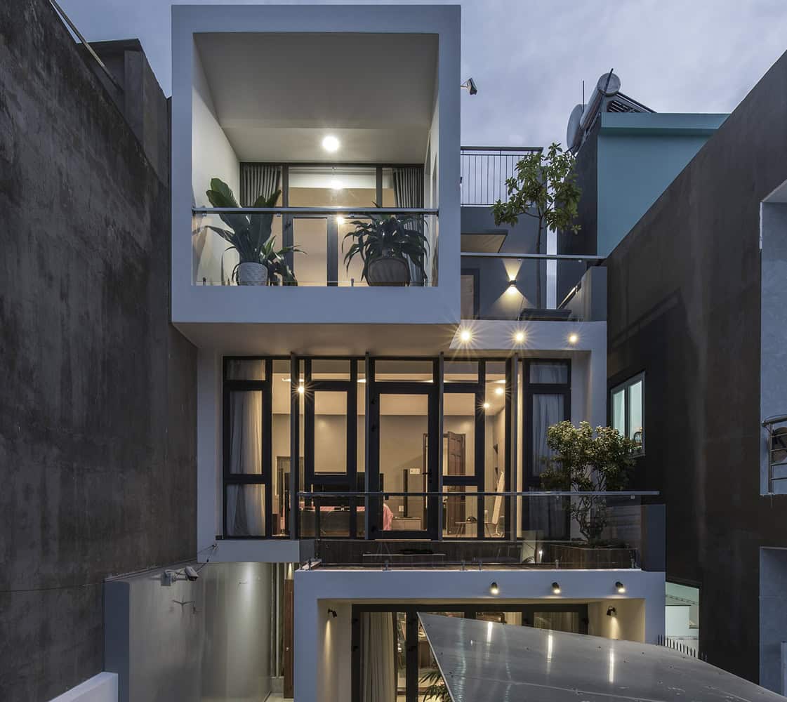 Modern multi-story house with large glass windows and balconies, illuminated at dusk, featuring contemporary architecture and stylish interior design elements.