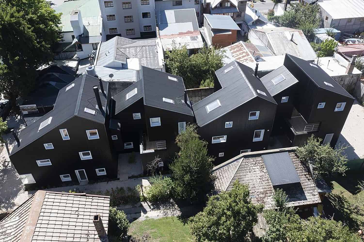 Modern black residential house with unique, angular architecture and multiple skylights in an urban neighborhood.