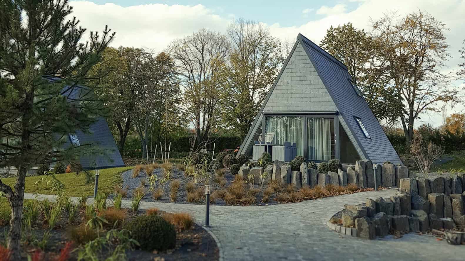 Stylish modern A-frame house with sleek gray exterior and large glass sliding doors, surrounded by landscaped gardens and trees, blending contemporary architecture with natural elements.