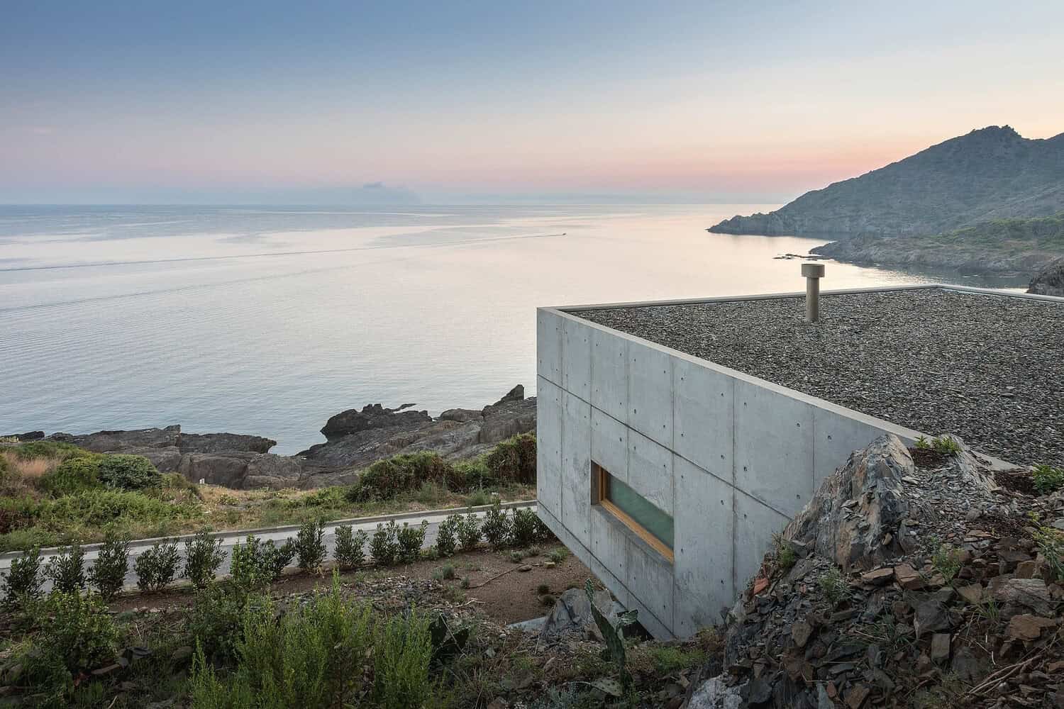Modern minimalist concrete house with flat roof overlooking ocean and rugged coastline, showcasing contemporary architecture and scenic seaside views.