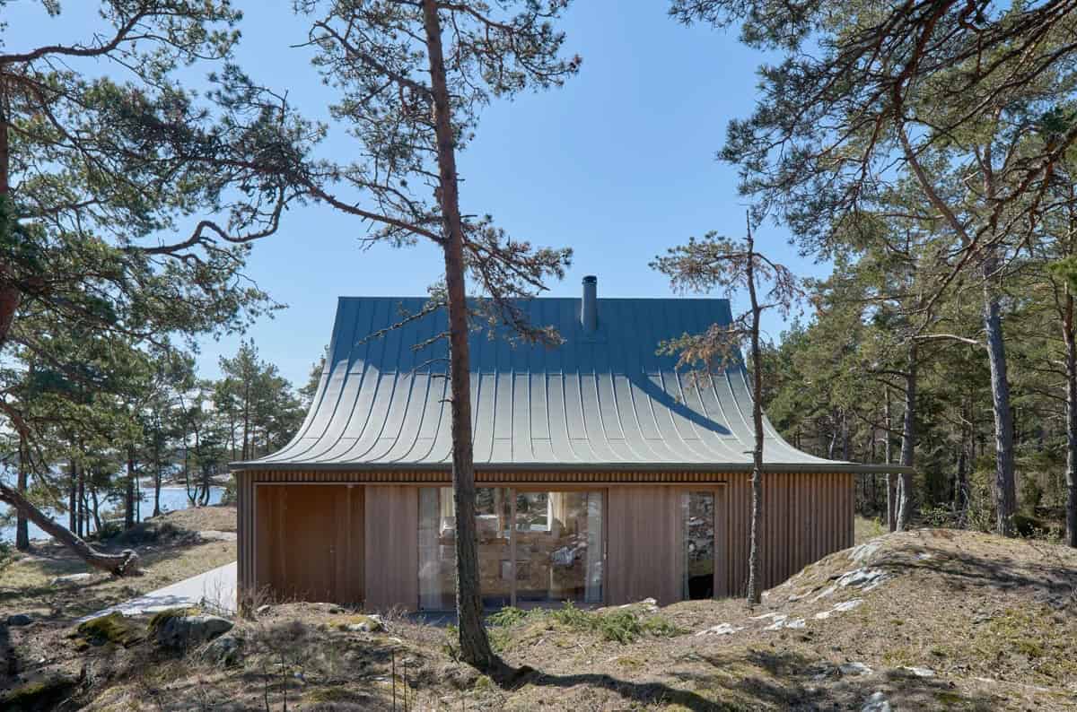 Rustic modern cabin with a unique metal roof surrounded by pine trees in a forest setting. Ideal for nature-inspired architecture and outdoor living, blending seamlessly with the natural environment.