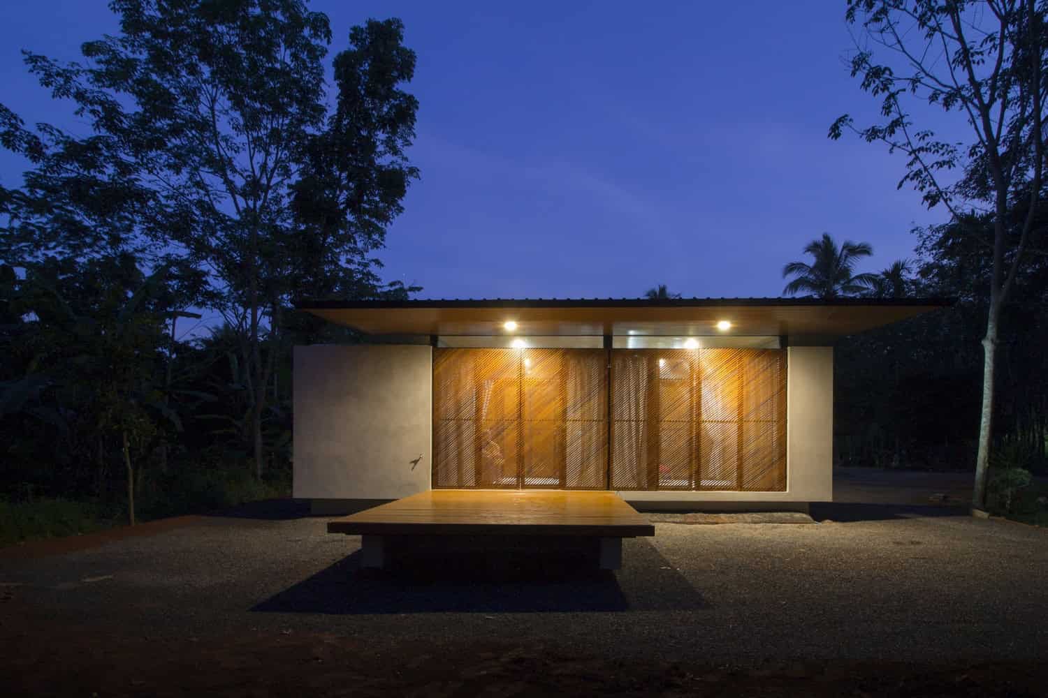 Modern minimalist tiny house with wooden accents and outdoor lighting, surrounded by lush trees, at dusk, showcasing innovative architecture and eco-friendly design.
