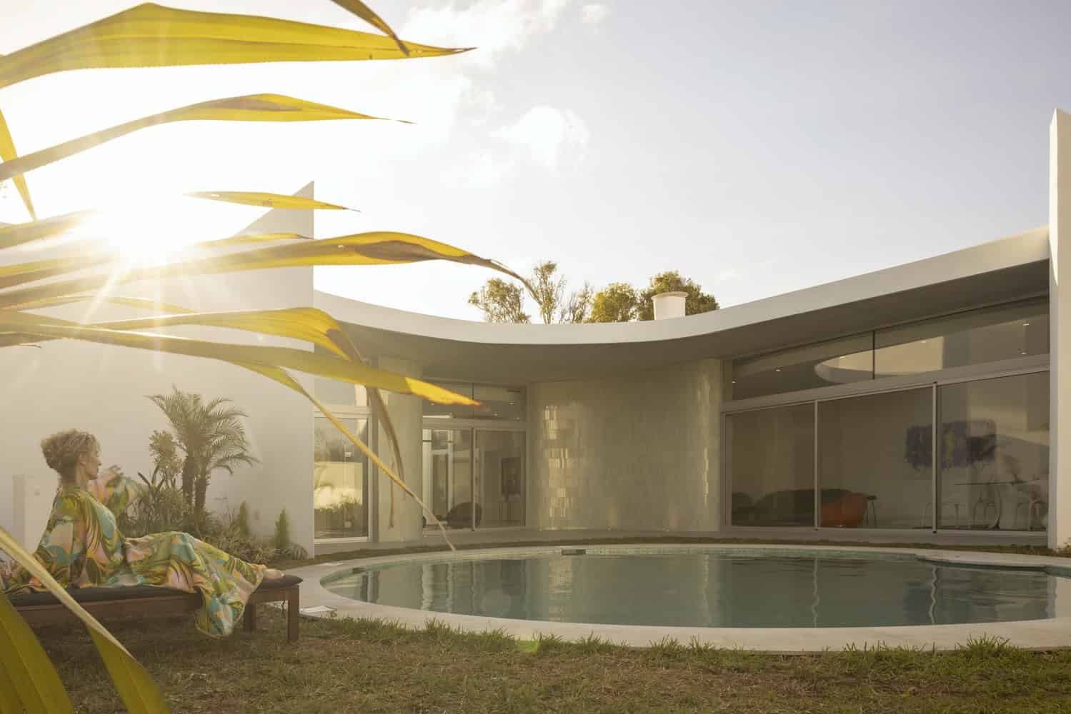 Modern luxury house with curved architecture and outdoor pool, set in a lush green landscape under bright sunlight, showcasing contemporary residential design and outdoor living space.