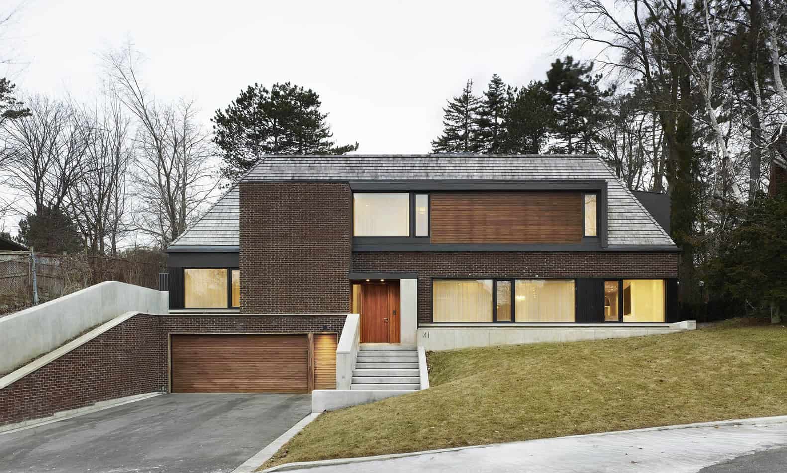 Contemporary modern house with brick and wooden exterior, large windows, and a sloped roof surrounded by trees, showcasing minimalist architectural design and curb appeal.