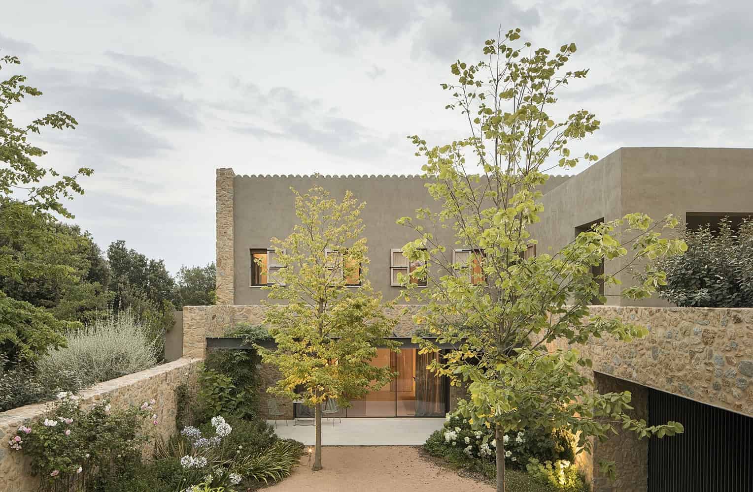 Contemporary modern house with stone and concrete facade, surrounded by lush greenery and trees, showcasing stylish architectural design and landscape integration for a sustainable living environment.