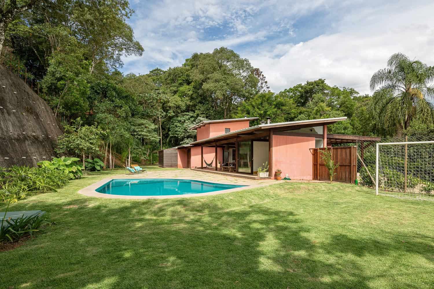 Modern mid-century house with a swimming pool surrounded by lush greenery and trees, showcasing contemporary architecture and outdoor landscaping.