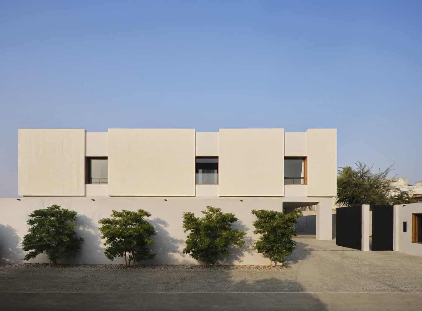Contemporary minimalist residential house with clean lines and geometric design, featuring neutral tones, modern windows, and surrounding greenery.