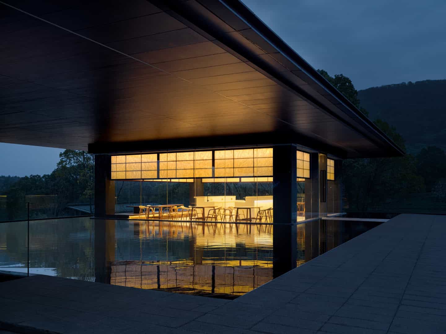 Modern architectural house with sleek design, illuminated interior, and infinity pool set against natural landscape, showcasing luxury home architecture and innovative building design.