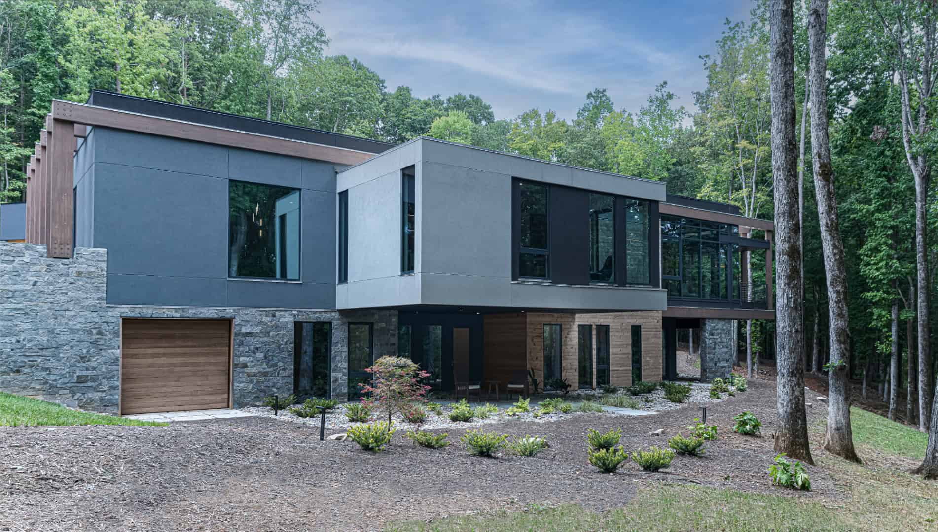 Modern luxury house with contemporary architectural design in a forest setting, featuring large glass windows, mixed materials, and natural landscaping.