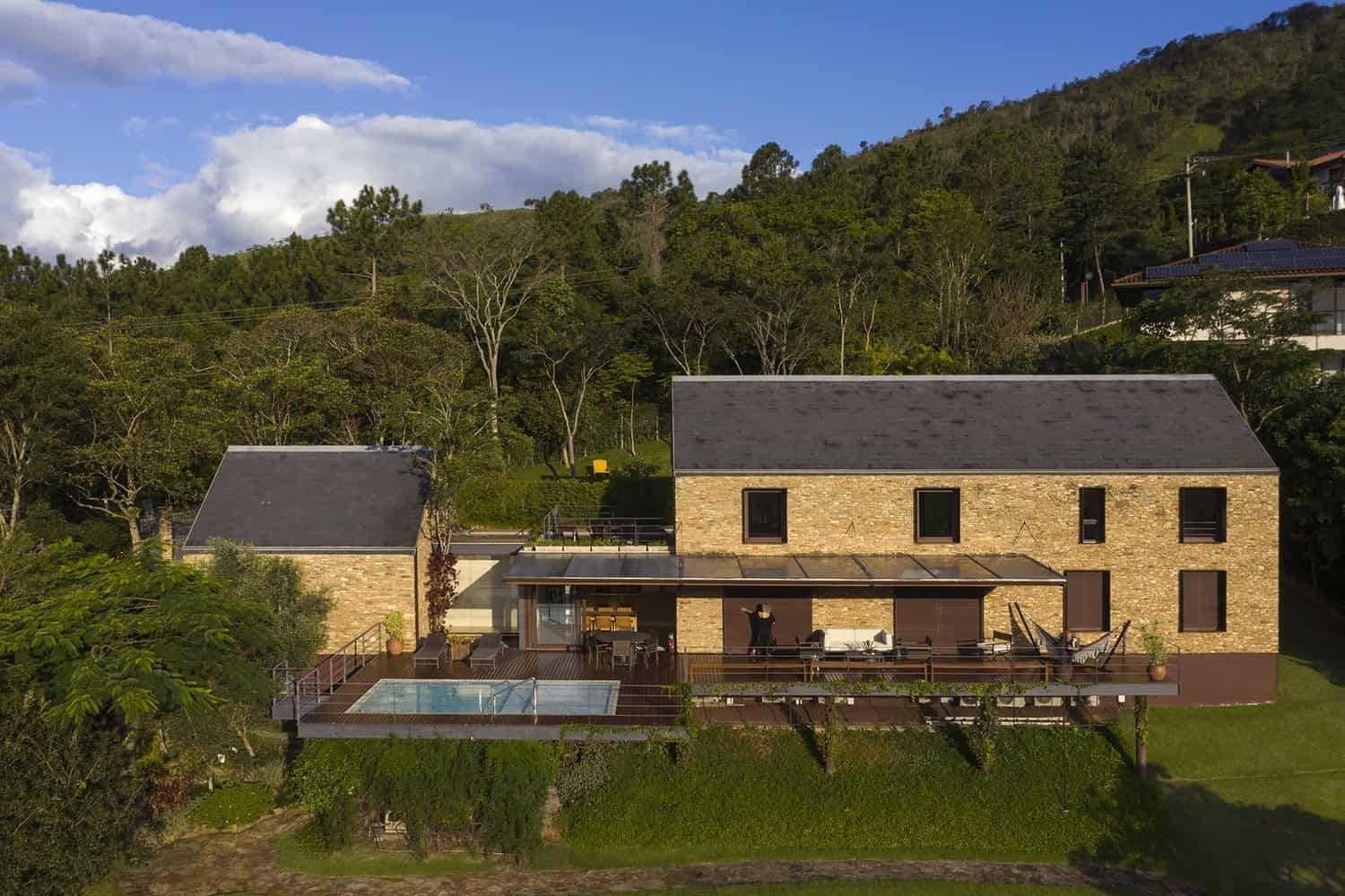 Modern mountain retreat with stone exterior, expansive deck, swimming pool, and panoramic views, blending contemporary architecture with natural landscape for a luxurious outdoor living experience.