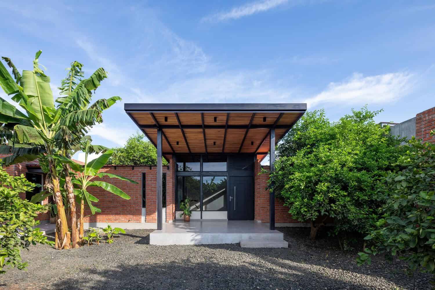 Modern minimalist house with brick exterior, wooden front porch, and surrounding lush greenery showcasing contemporary architecture design.