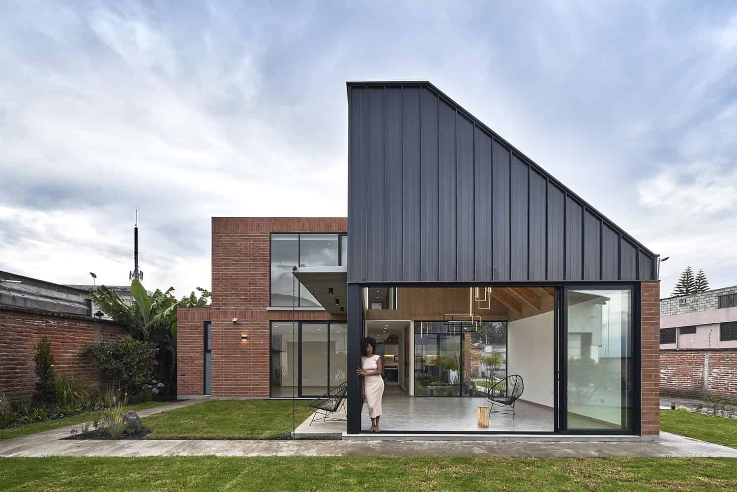 Contemporary modern house with red brick exterior, black metal cladding, large glass windows, and open interior design, showcasing sleek architectural details and modern landscaping.