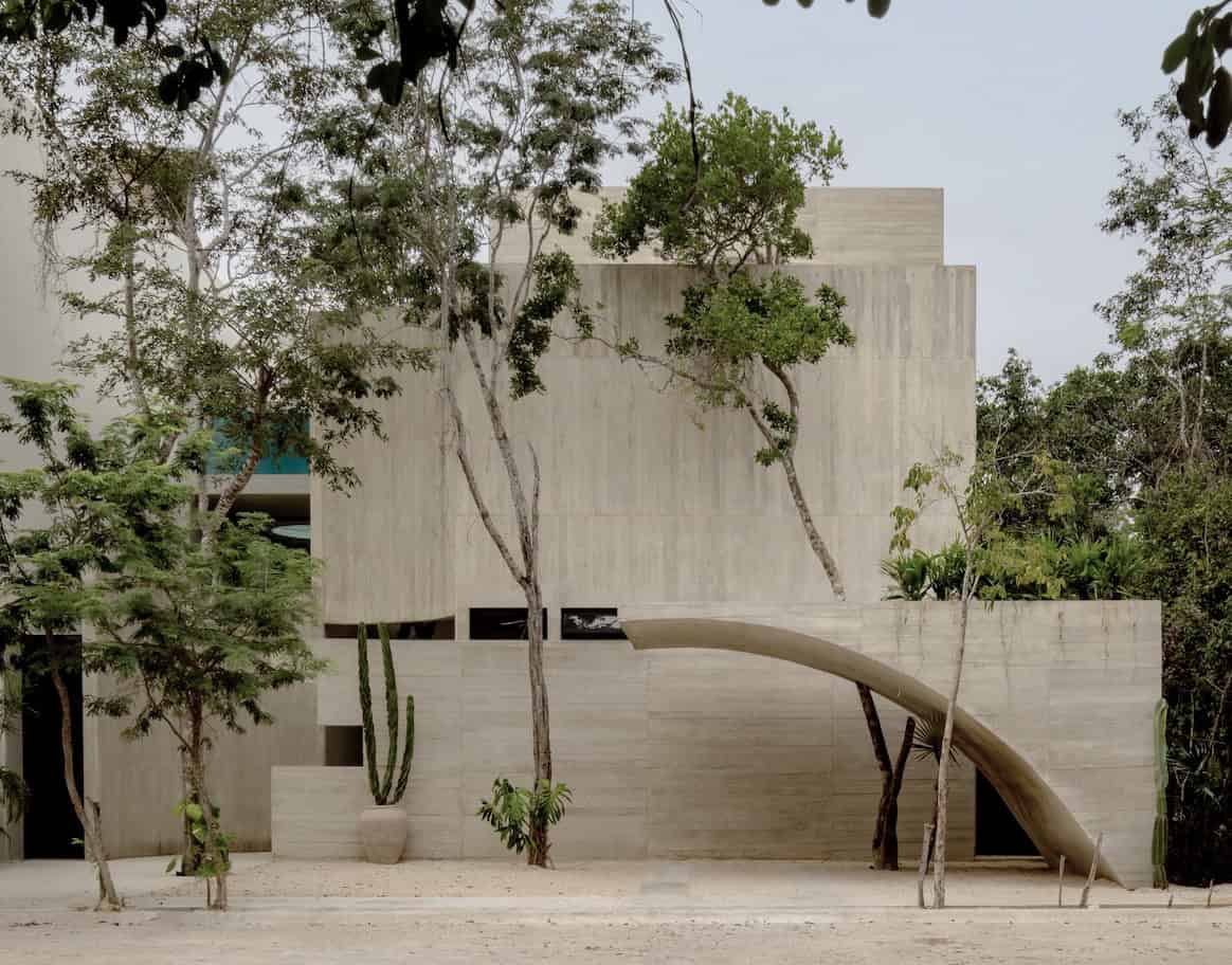 Modern minimalist concrete house with curved architectural features and lush greenery, showcasing contemporary architectural art designs and innovative home architecture.